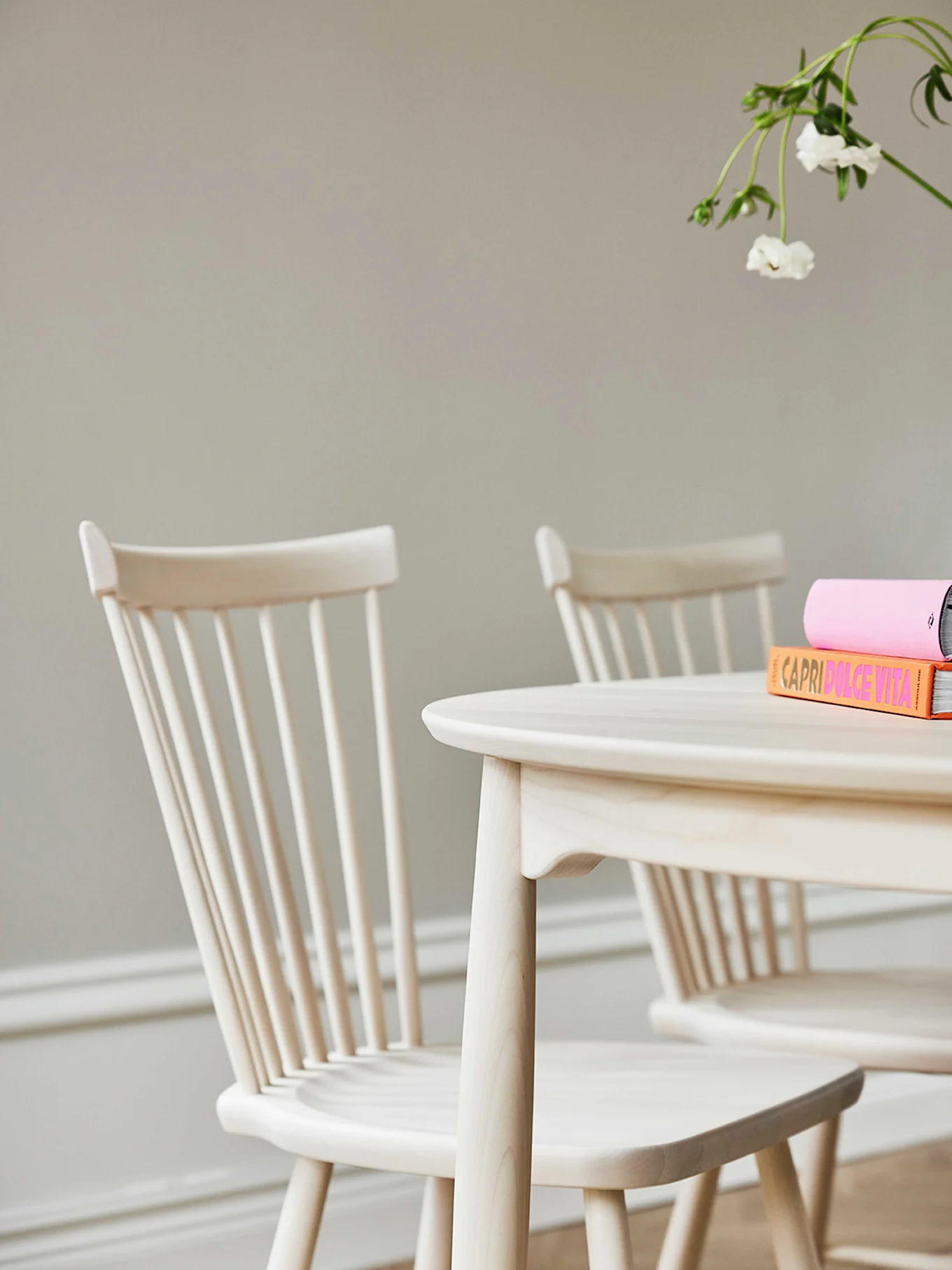 Matbord och stolar i ljust trä med böcker och en vit blomma.