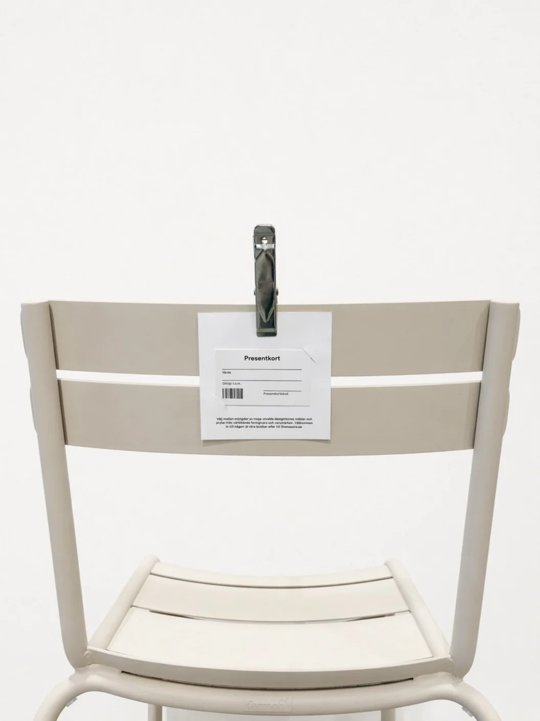 Ljusbeige stol med ett presentkort fäst vid ryggstödet med en metallklämma.