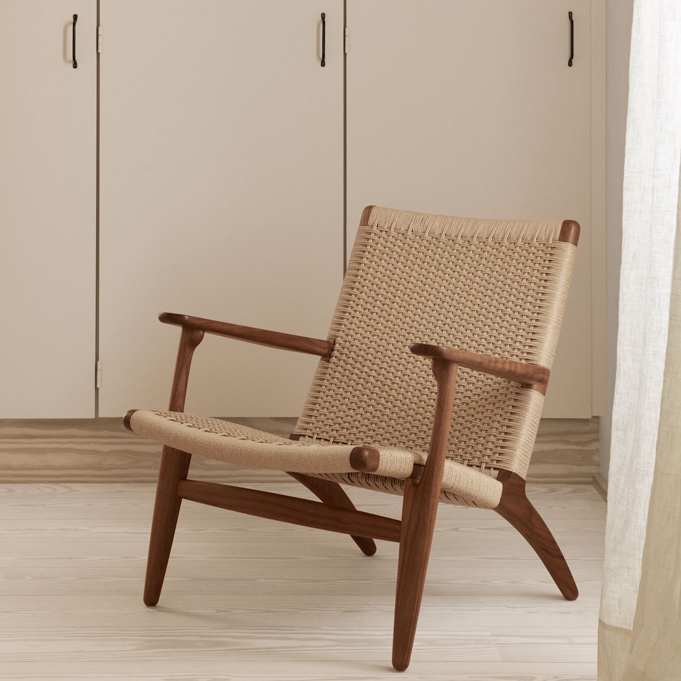 En stol med intressant profil, CH25 fåtölj från Carl Hansen & Søn är formgiven av Hans J. Wegner och har en vackert flätad sits med stomme i trä, här visas en variant i oljad valnöt med naturfärgad sits, placerad framför garderobsvägg.