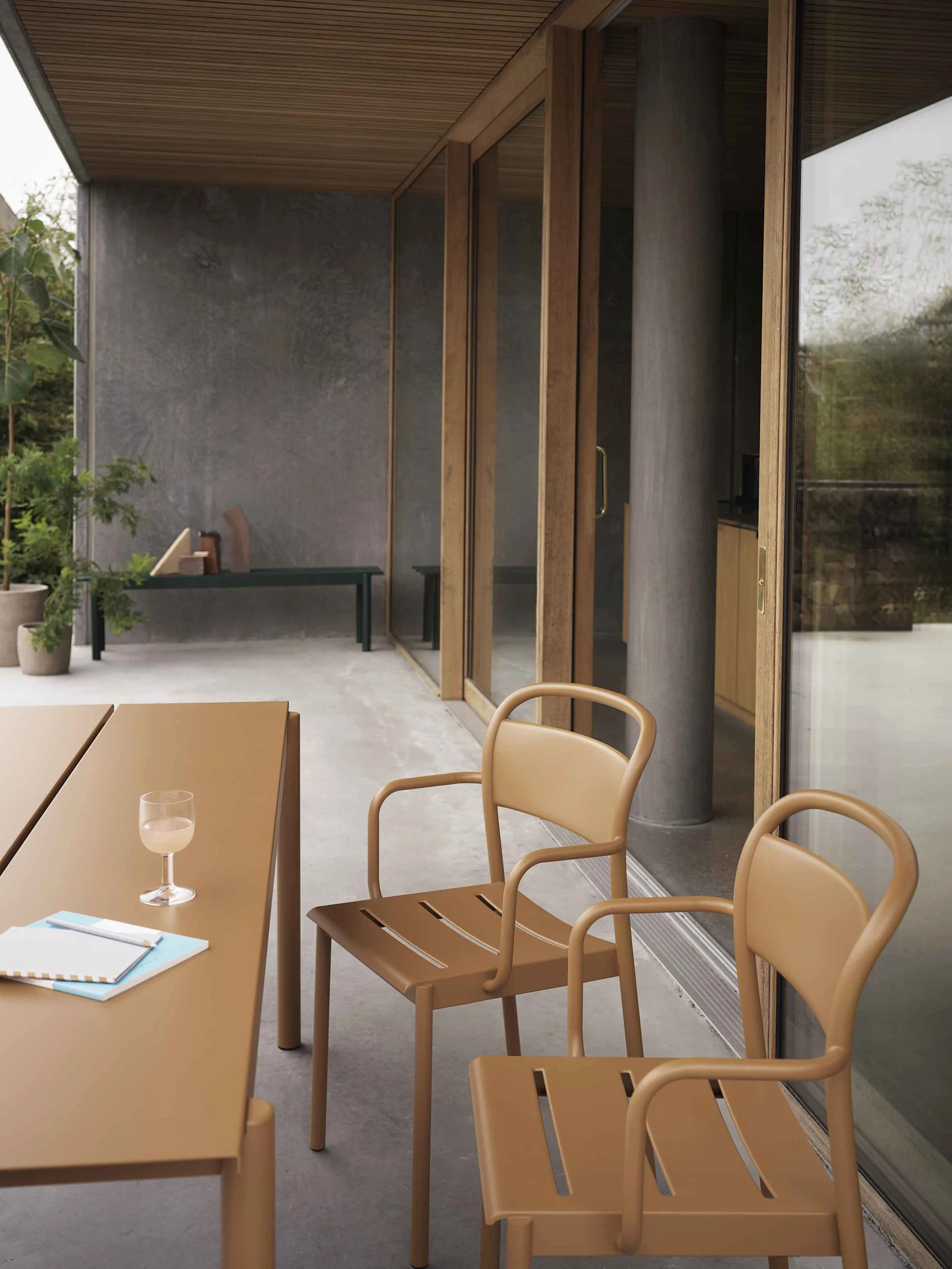 Uteplats med brunt/tan bord och två matchande stolar med rundade ramar och springor i sätet, framför skjutdörrar i glas.