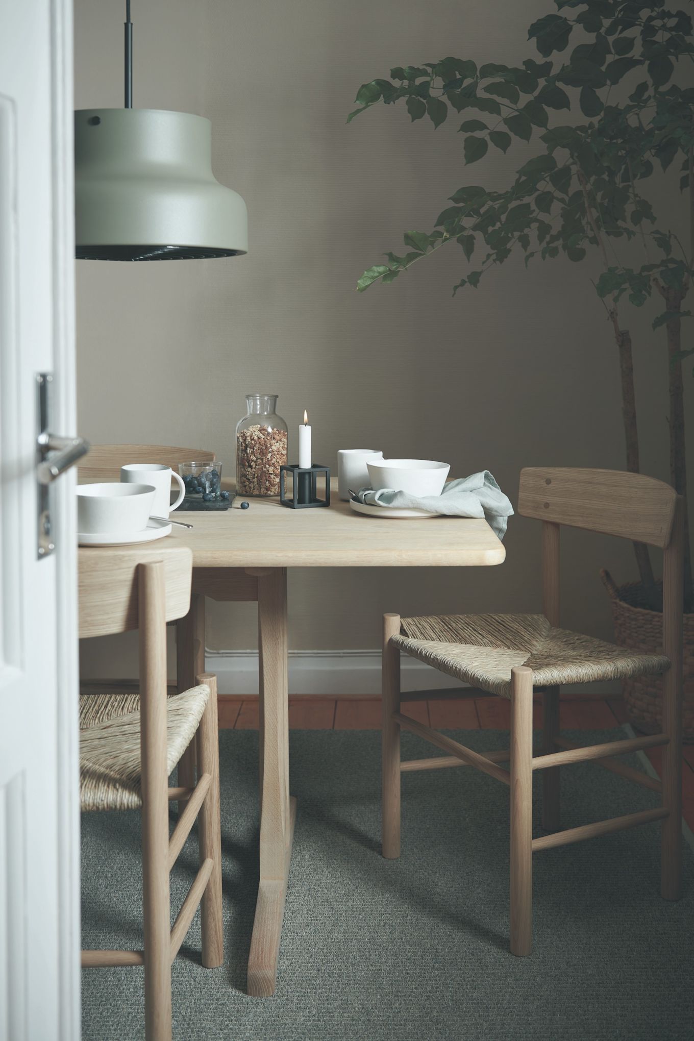 Matplats-inspiration med en dukning i naturlig stil med ekbord och ekstol från Fredericia Furniture och porslinsserien Sandsbro i vitt från Scandi Living, över bordet hänger en grön Bumling-lampa från Atelje Lyktan.