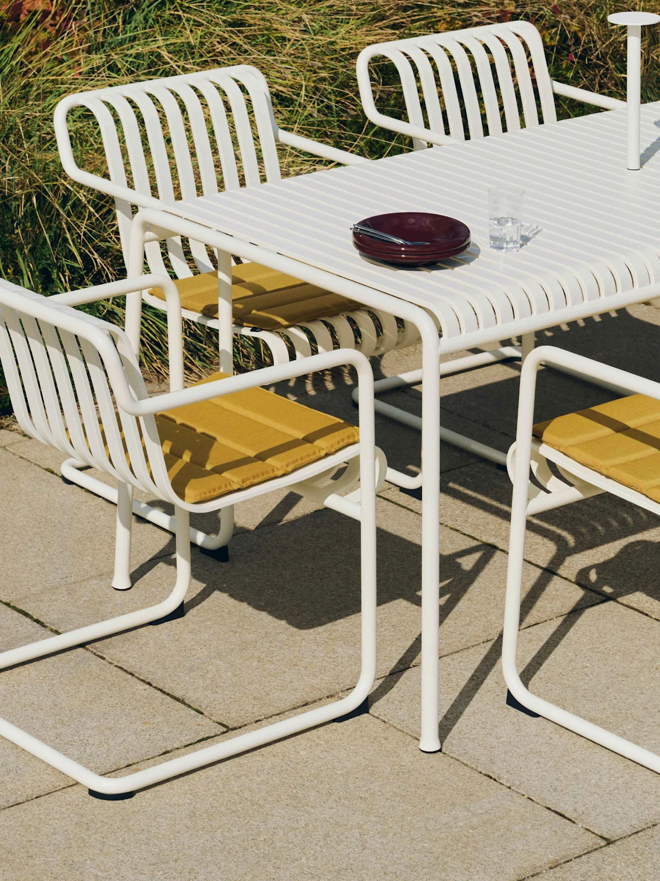 Vitt ribbbord med matchande stolar, gula dynor och servis på en uteplats.